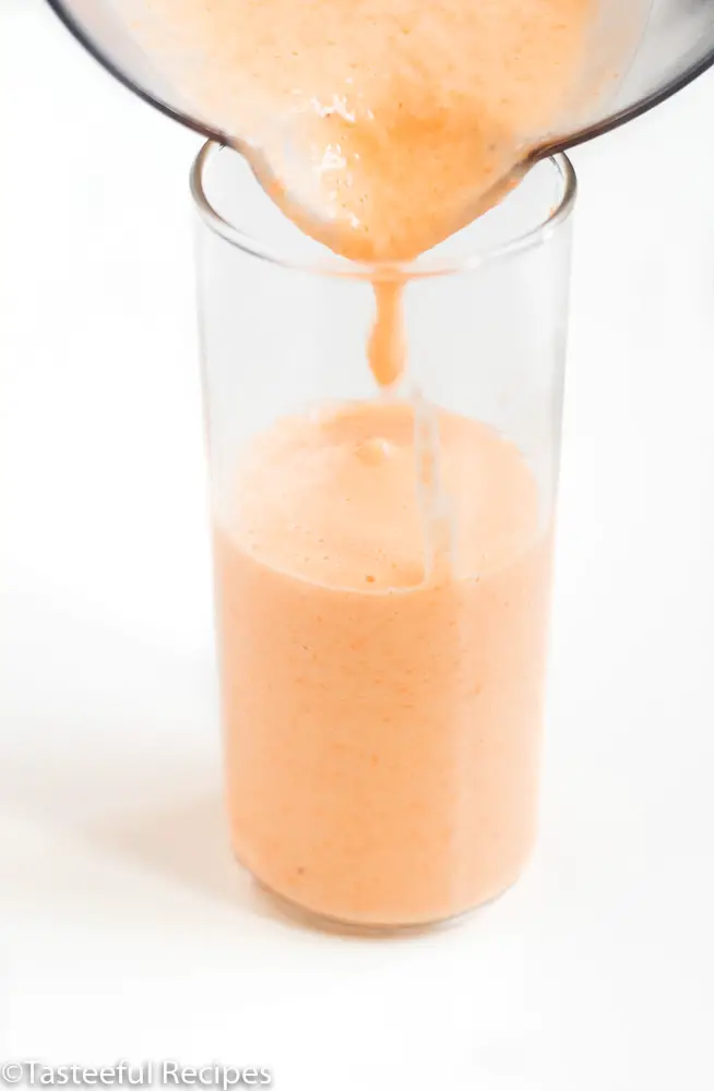 Straight on shot of a carrot smoothie being poured into a glass