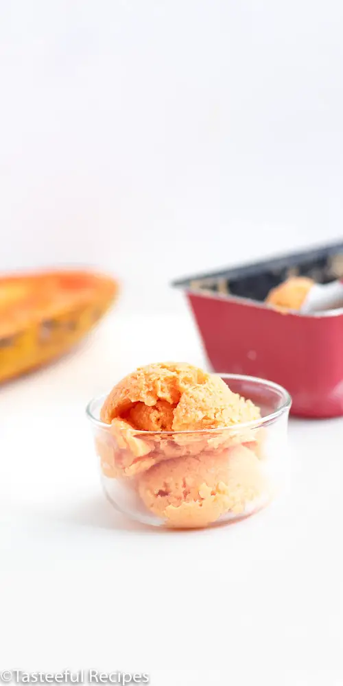 Straight on shot of no-churn papaya frozen yogurt in a glass bowl with a slice of a papaya in the background