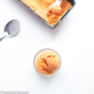 Overhead shot of no-churn papaya frozen yogurt in a glass bowl with a spoon and a loaf pan in the background