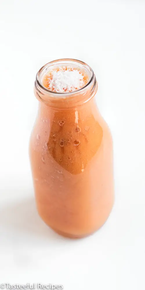 Angled shot of a dairy free papaya smoothie in a glass bottle topped with shredded coconut