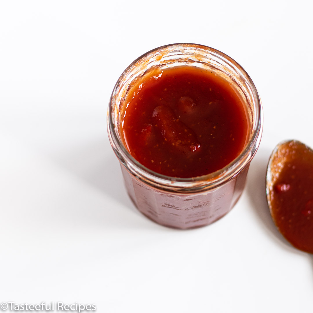 Overhead shot of a spicy pineapple bbq sauce in a jar with a spoon on the surface