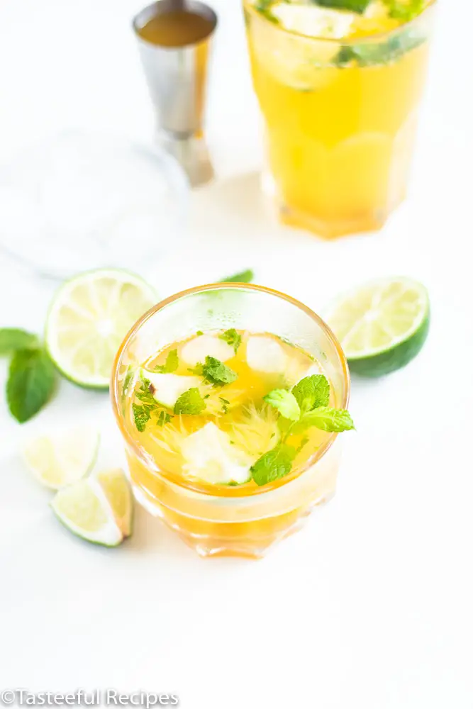 Angled shot of two virgin passion fruit mojitos in glasses garnished with mint leaves and lime wedges