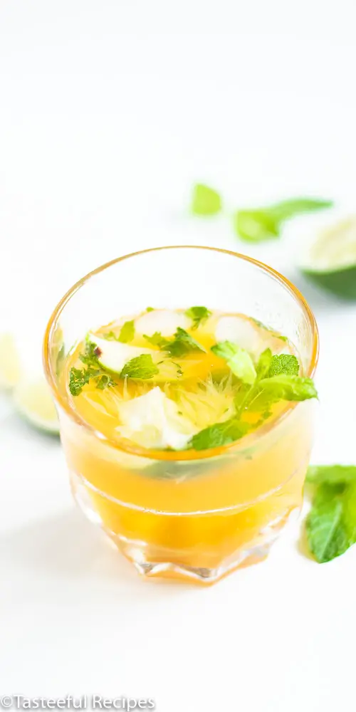 Angled shot of a virgin passion fruit mojito in a glass garnished with mint leaves and lime wedges