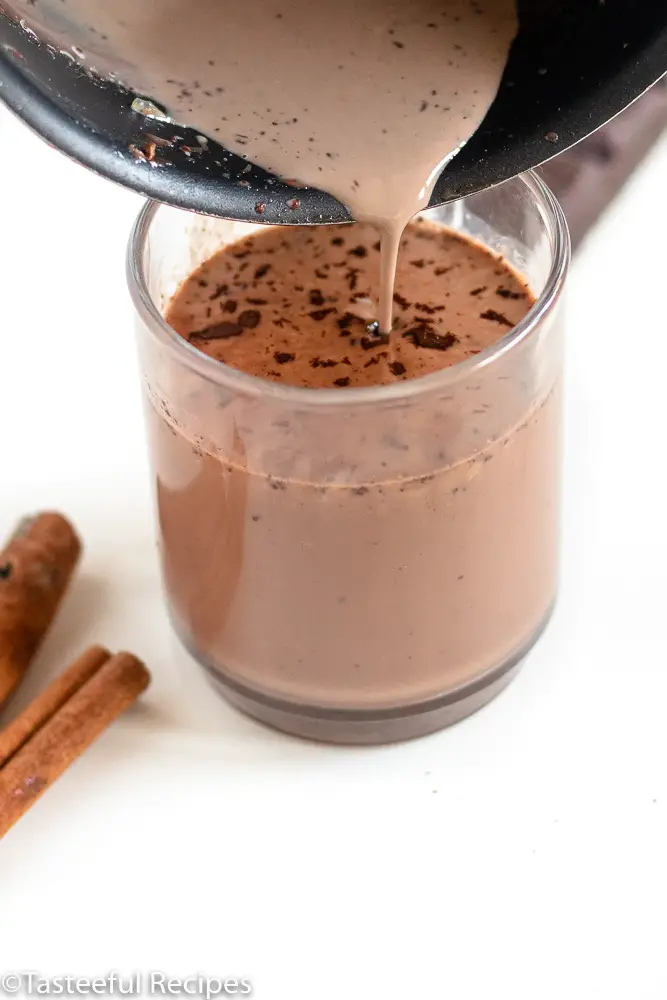 Angled shot of creole hot chocolate being poured into a glass mug