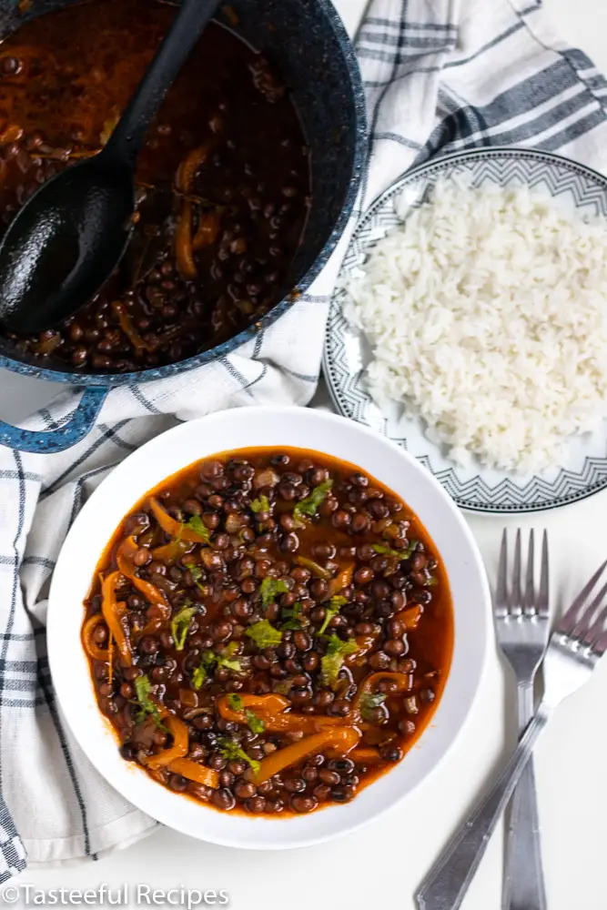 Overhead shot of a plate filled with stewed pigeon peas, another plate of rice and a pot of stewed pigeon peas