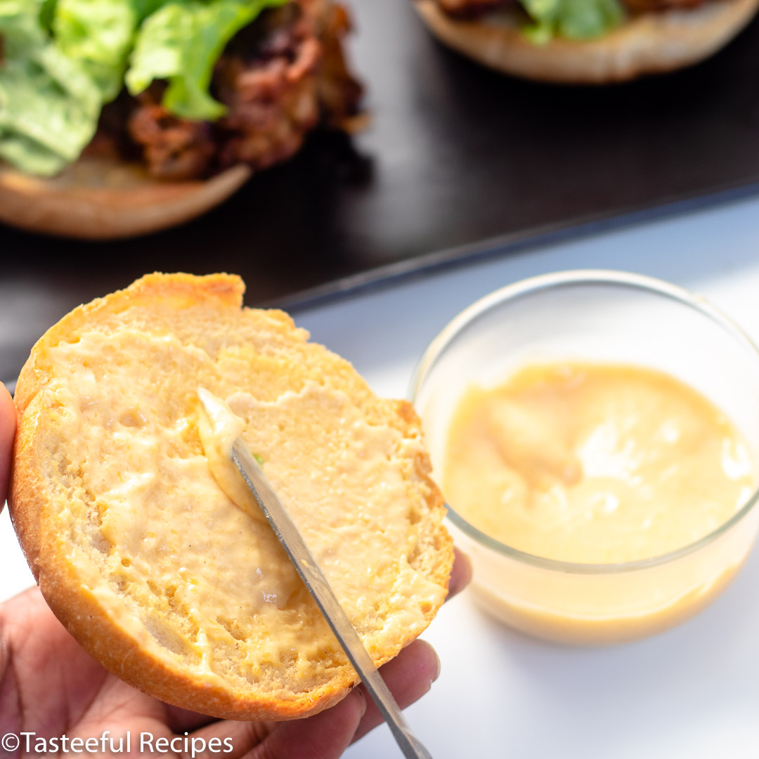 Angled shot of a burger bun being dressed with spicy mango mayo