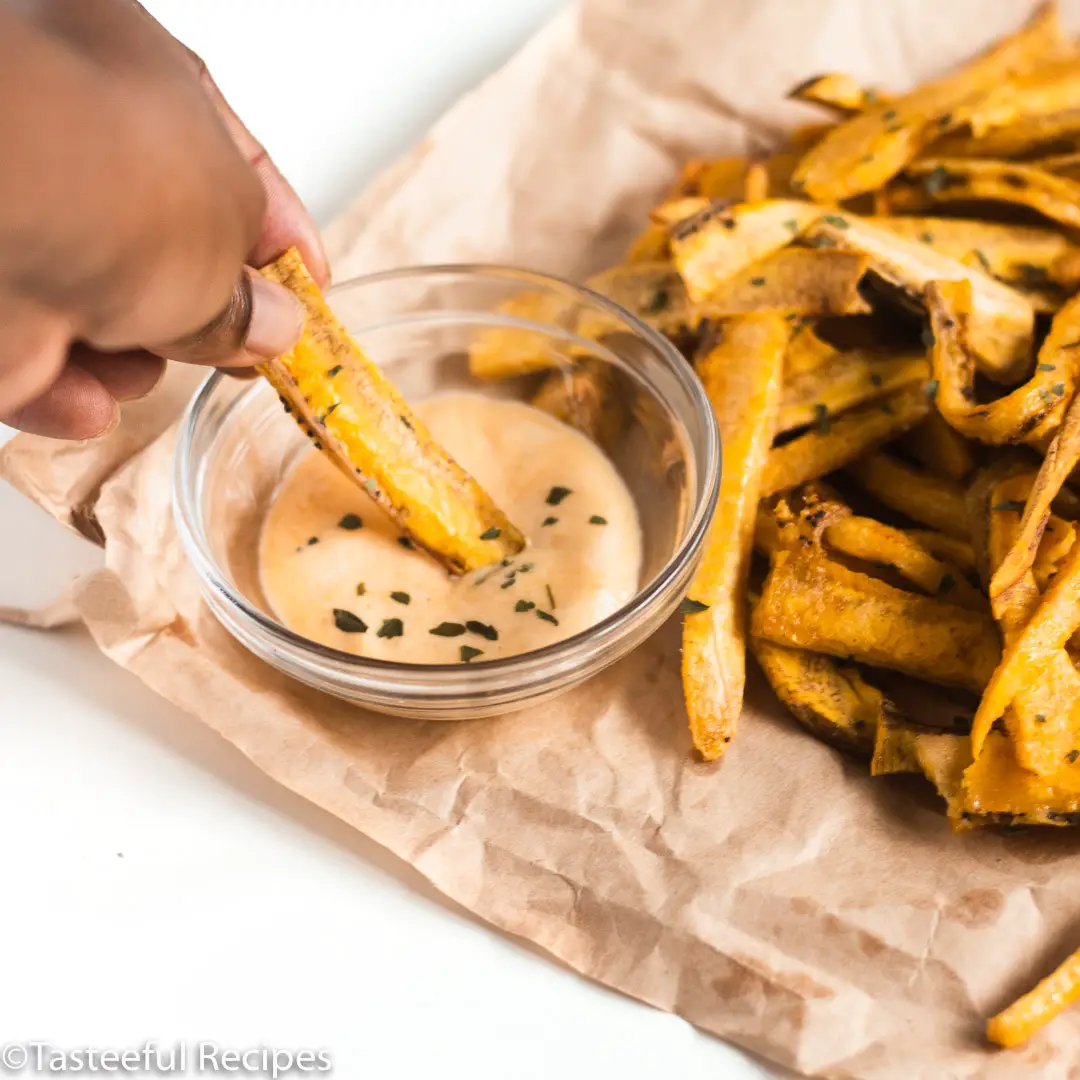 Angled shot of a hand dipping a plantain fries into a sauce