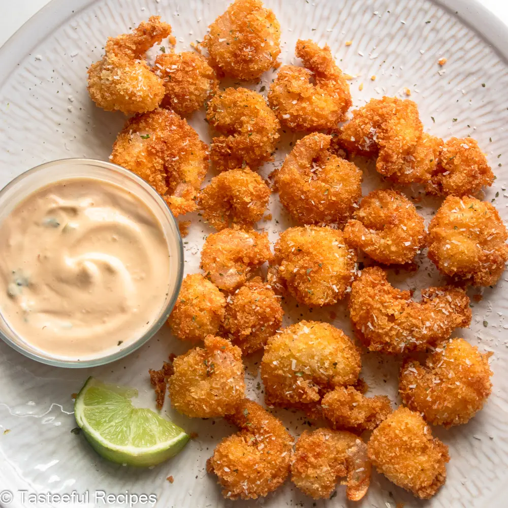 Overhead shot of a plate of fried coconut crusted shrimps with a shrimp cocoktail sauce and a wedge of lime