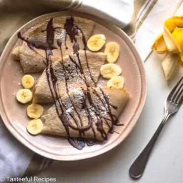 Overhead shot of banana repes on a plate drizzled with chocolate syrup and slices of banana